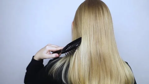 Back view. Blonde runs a comb through her straight golden hair. Hair care concep Stock Footage 302257453