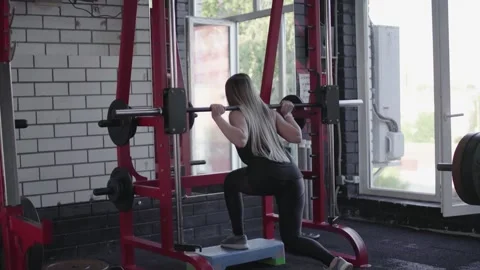 Back view of blonde woman does Lunges squats with barbell on smith machine Stock Footage 143520125