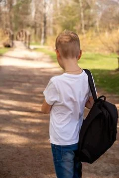 Back view of a boy with backpack walking on a path in the park Stock Photos