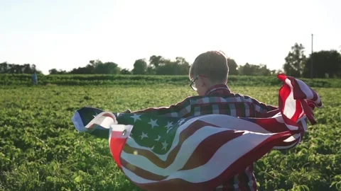 Back view of a boy holding USA flag wrapped around shoulders at sunset. Vídeos de archivo 341483893
