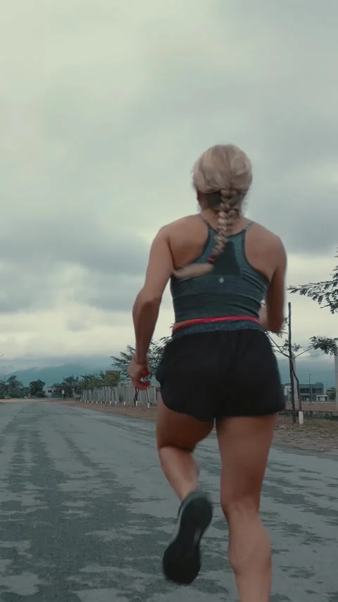 Back view of braided female runner on a tree lined road Stock Footage 340046891
