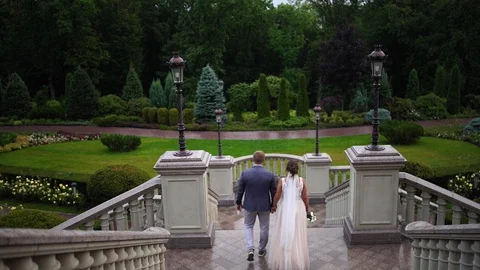Back view. The bride and groom hold hands and go down the stairs. Stock Footage 129114658