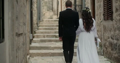 Back view of bride in beautiful white dress and groom walking in Europe old town Stock Footage 130581716