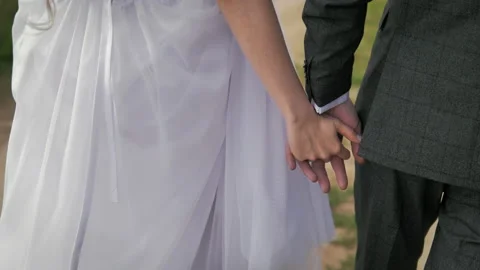Back view of bride in beautiful white dress and groom in a suit go holding hands Stock Footage 131396021