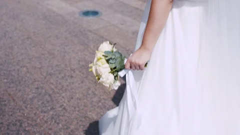 Back view of bride in dress walking and carrying bouquet of flowers on street Stock Footage 285346427