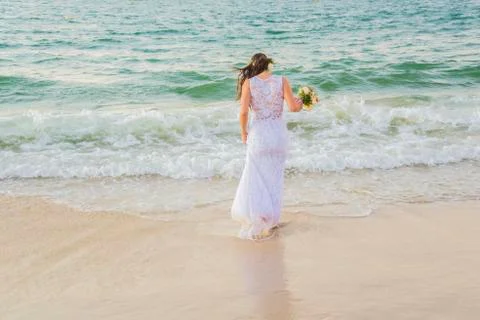 Back view of bride entering the sea with wedding dress and bouquet in hand. Stock Photos