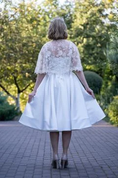 Back view of a bride holding the sides of her flowing tea-length wedding dress,  Stock Photos