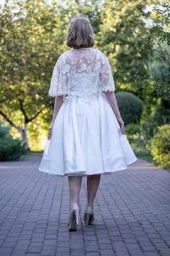 Back view of a bride holding the sides of her flowing tea-length wedding dress,  Stock Photos