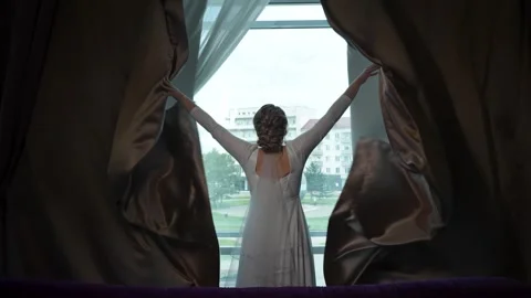 A back view of a bride in wedding dress opening curtains in front of the window 動画素材 295453816