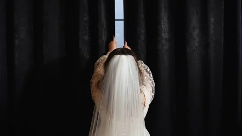 Back view of a bride in a white dress opening black curtains to the sides Stockbeeldmateriaal 312627635