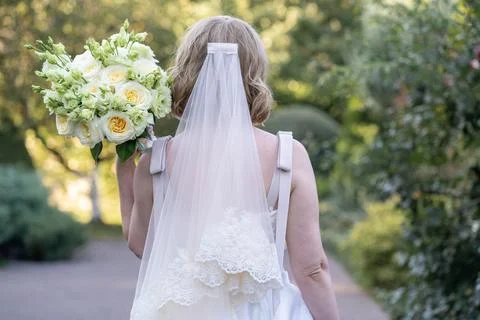 Back view of a bride in a white wedding dress with a long veil, holding an elega Stock Photos