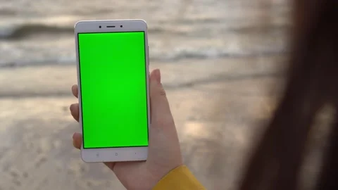 Back view of brunette holding chroma key green screen smartphone watching Stock Footage 133918572