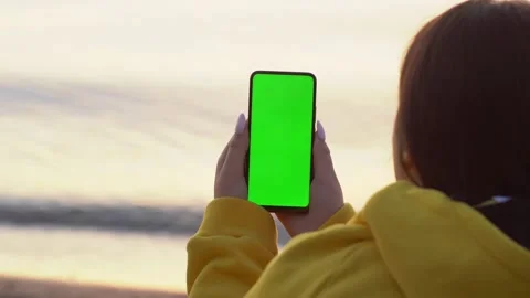 Back view of brunette holding chroma key green screen smartphone watching Stock Footage 140989776