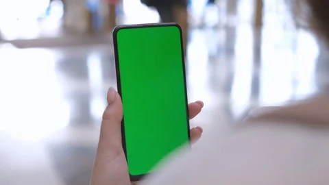 Back view of brunette holding chroma key green screen smartphone watching Stock Footage 241378043