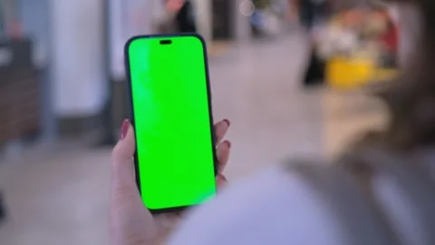 Back view of brunette holding chroma key green screen smartphone watching Stock Footage 266421294