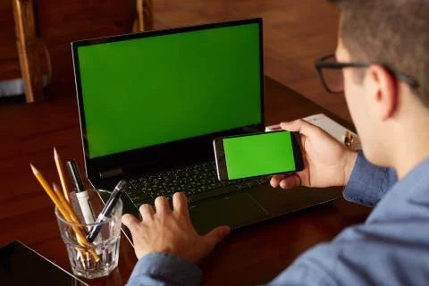 Back view of businessman using smartphone and laptop typing in office. Green Stock Photos