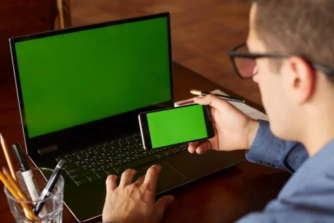 Back view of businessman using smartphone and laptop typing in office. Green Stock Photos