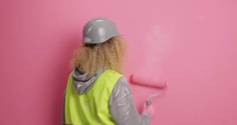Back view of busy female painter does repair of apartment paints wall in pink Stock Footage 155856344