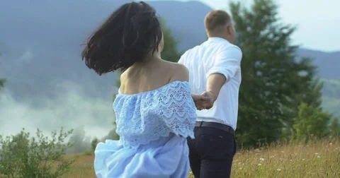 The back view of the cheerful young couple holding hands while running along the Stock Footage 82795620