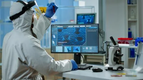 Back view of chemist man in coverall typing on computer analysing vaccine Stock Photos