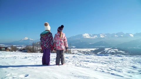 Back view of children standing on rural roadway in snow looking at mountain 스톡 동영상 105700637