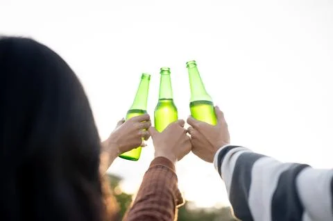 Back view close up of man and woman friends raising drink bottle in a field.. Stock Photos