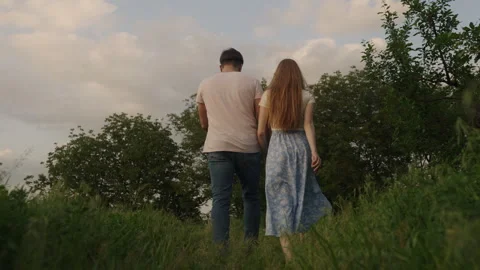 Back view of a couple hand in hand romantic walk by the summer valley in the Stock Footage 246275558