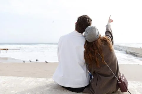 Back view of couple sitting on the beach in autumn Stock Photos