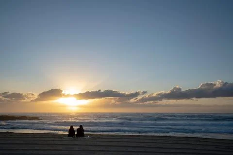 Back view of a couple sitting on the sandy beach watching the sea during cloudy Stock Photos