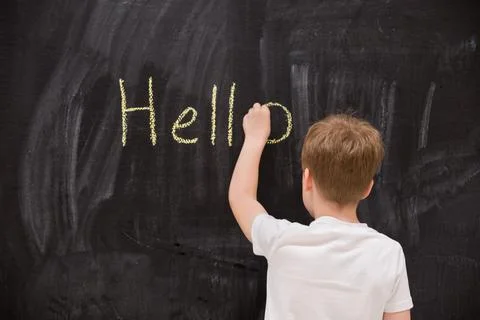Back view on cute kid boy writing Hello word with chalk on the backboard in s Stock Photos