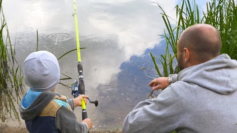 Back view of dad and small son fishing from the bank on river Stock Footage 93049175