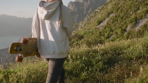 Back view of  dreadlocks woman walking with skateboard on mountain on sunny day Stock Footage 134809504
