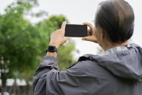 Back view of elderly man holding a mobile phone to take photo at park in th.. Stock Photos