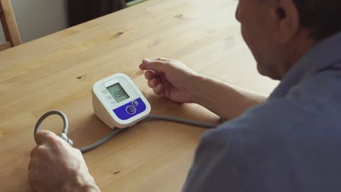 BACK VIEW: An elderly man measuring the blood pressure at home Vídeos de archivo 143884568