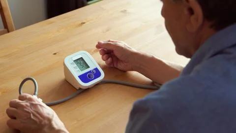 BACK VIEW: Elderly man measuring the blood pressure at home Stock Photos