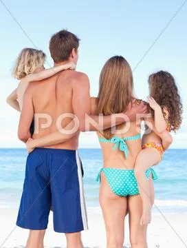 Back View Of Family Standing On The Beach