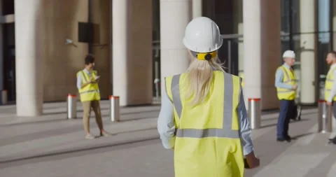 Back view of female engineer in safety hardhat and vest entering office building Stock Footage 156445234