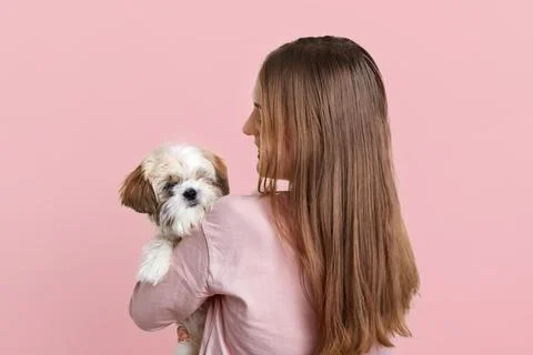Back view of female with long dark hair, carries little fluffy dog, plays a.. Stock Photos