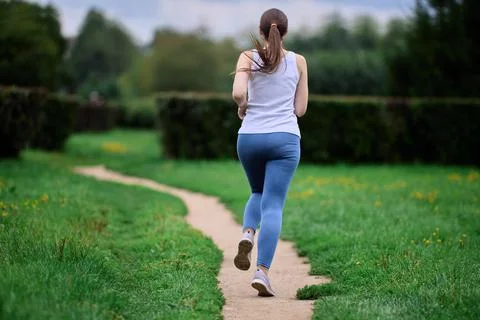 Back view of female runner exercising in public park in summer. 写真素材
