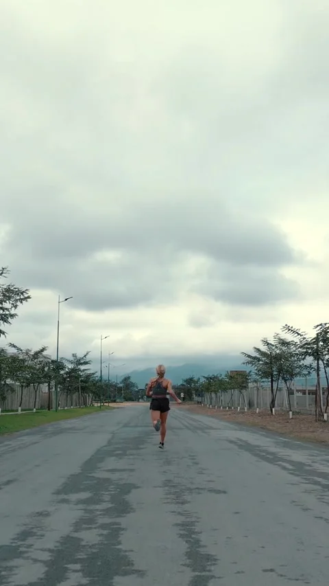 Back view of female runner receding down a long straight road Stock Footage 340046976