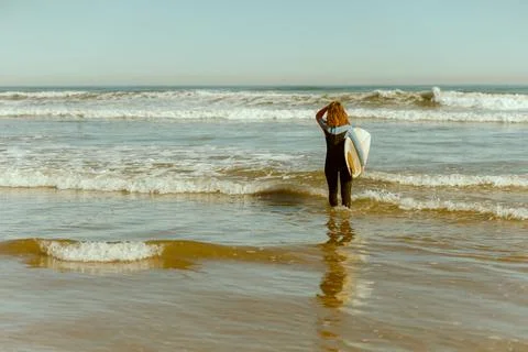 Back view of female surfer in wetsuit with his surfboard entering the sea for Stock Photos