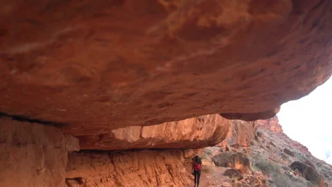 Back View of Female Trekker With Backpack Walking Beneath Red Rocks on Video stock 233005610