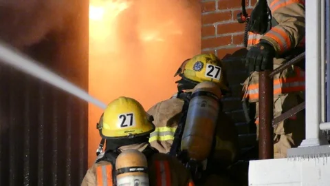 Back view of firemen on stairs spraying water into windows Stock Footage 85366553