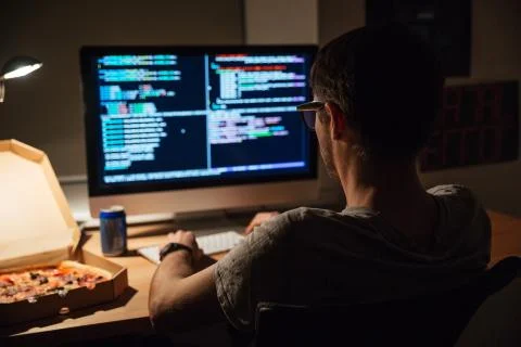 Back view of focused programmer writing code and eating pizza Stock Photos