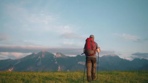 Back view following man walking on meadow hill overlooking mountain peaks Stock Footage 283028655
