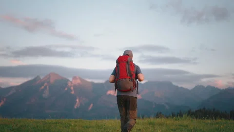 Back view following man walking on meadow hill overlooking mountain peaks Stock Footage 283029157