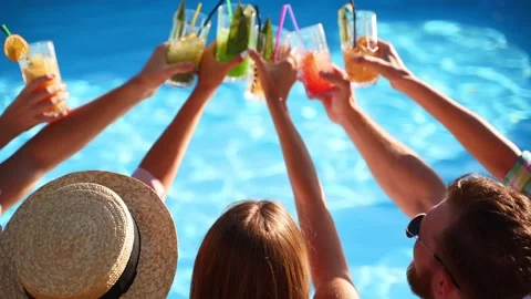 Back view of friends clinking glasses with cocktails sitting by swimming pool on Stock Footage