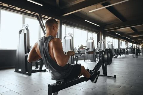 Back view of full length man exercising in gym using ergometer or rowing machine Stock Photos