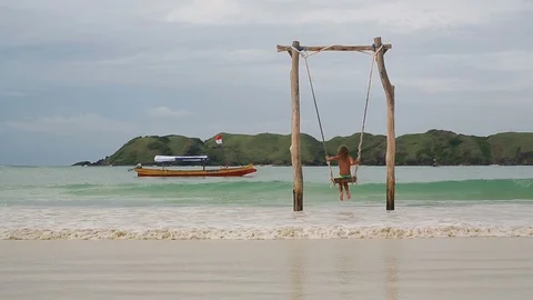 Back view of the  girl having fun swinging at tropical island beach  Stock Footage 102562722