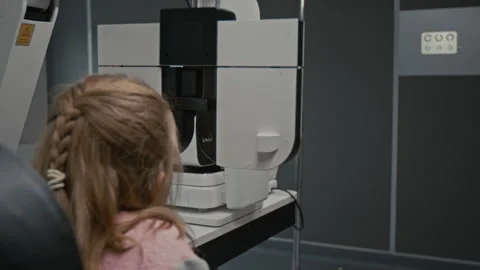 Back View Girl Looking into Phoropter During Eye Exam Stock Footage 322693682